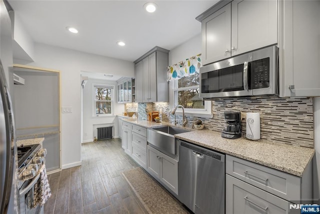 kitchen with radiator, a sink, decorative backsplash, gray cabinetry, and appliances with stainless steel finishes