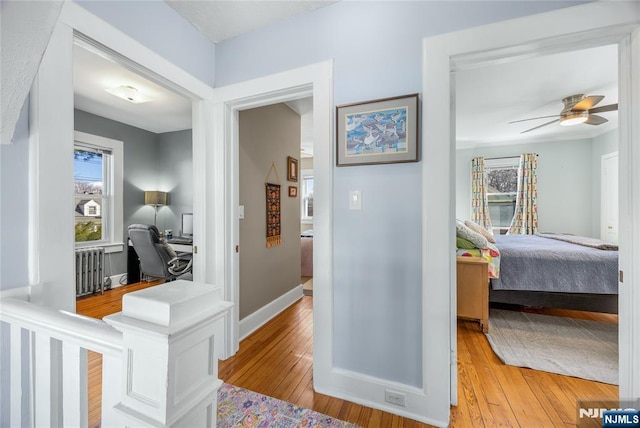 corridor featuring radiator heating unit, light wood-style floors, baseboards, and a healthy amount of sunlight