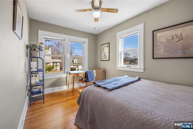 bedroom featuring light wood-style flooring, radiator, a ceiling fan, and baseboards