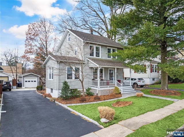 view of front of home with a front yard, covered porch, a garage, an outbuilding, and driveway