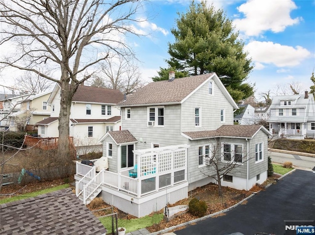 rear view of house featuring a shingled roof, a wooden deck, a residential view, and a chimney