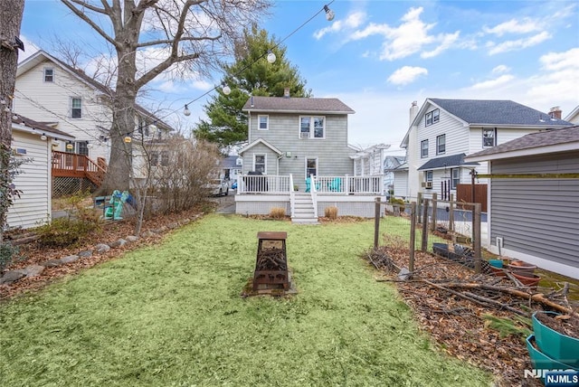 rear view of house with a wooden deck, a fire pit, a lawn, and fence