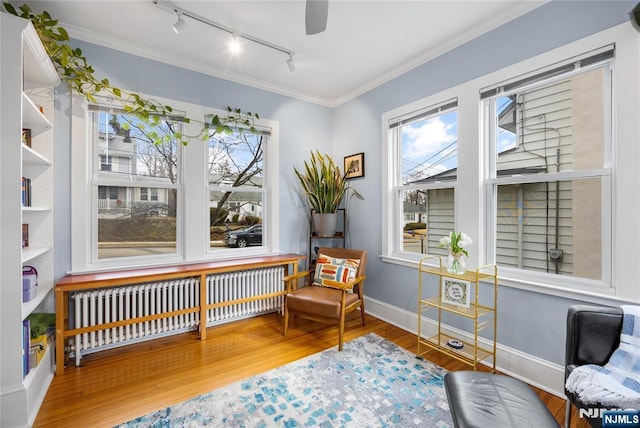 living area featuring a healthy amount of sunlight, crown molding, radiator heating unit, and wood finished floors