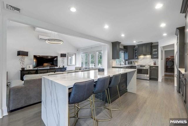 kitchen featuring visible vents, wood finished floors, open floor plan, stainless steel appliances, and vaulted ceiling