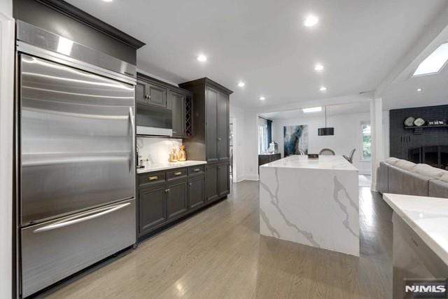 kitchen with built in refrigerator, open floor plan, recessed lighting, light wood finished floors, and light stone countertops