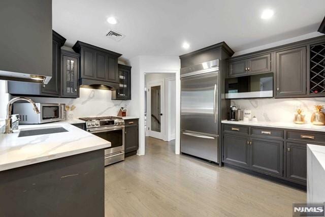 kitchen with visible vents, backsplash, light wood-type flooring, appliances with stainless steel finishes, and a sink