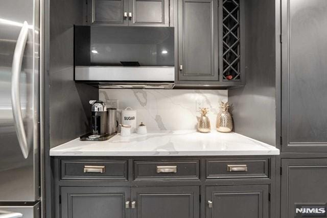 kitchen featuring decorative backsplash, gray cabinetry, light stone countertops, and stainless steel appliances