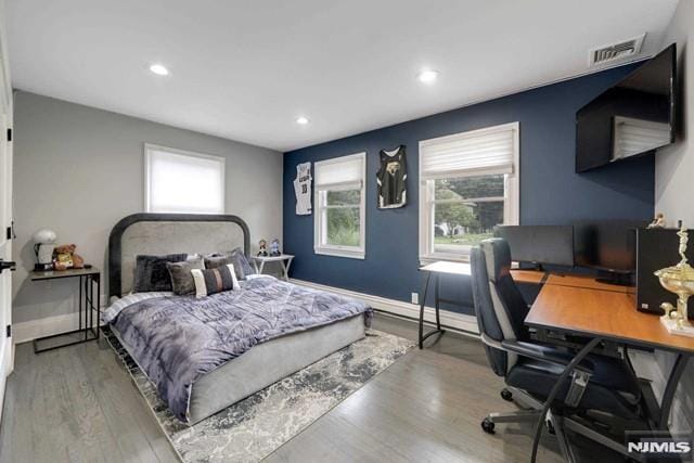 bedroom featuring visible vents, multiple windows, baseboards, and wood finished floors