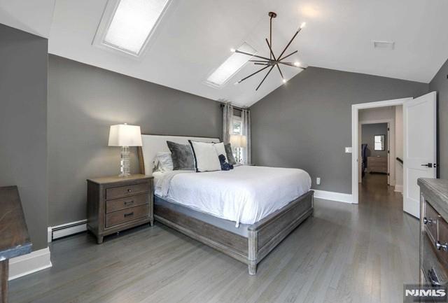 bedroom with a baseboard heating unit, lofted ceiling, light wood-type flooring, and a chandelier