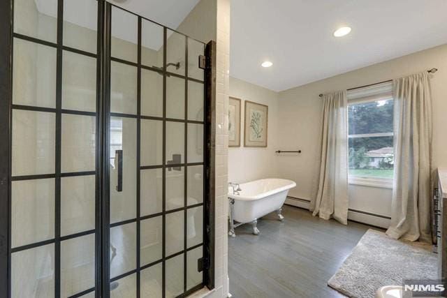 full bathroom with a baseboard heating unit, wood finished floors, a tile shower, and a freestanding bath