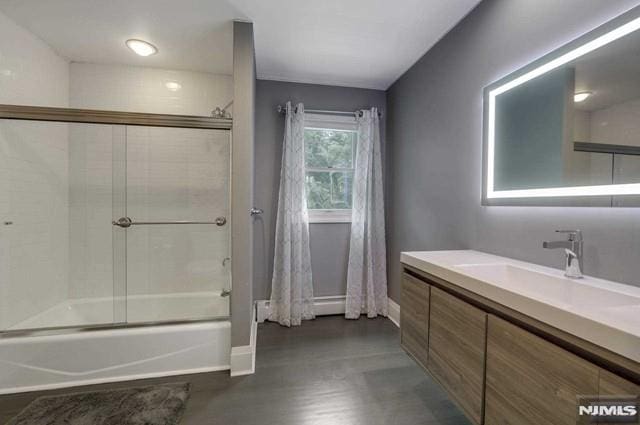 full bath with vanity, baseboards, and combined bath / shower with glass door