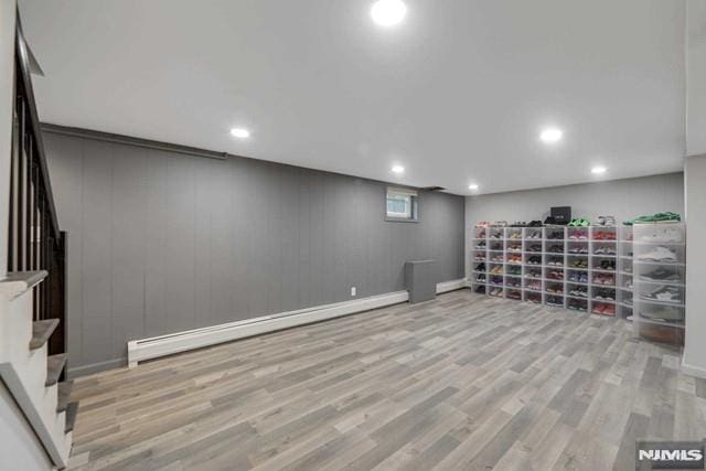 finished below grade area featuring recessed lighting, a baseboard heating unit, wood finished floors, and stairway