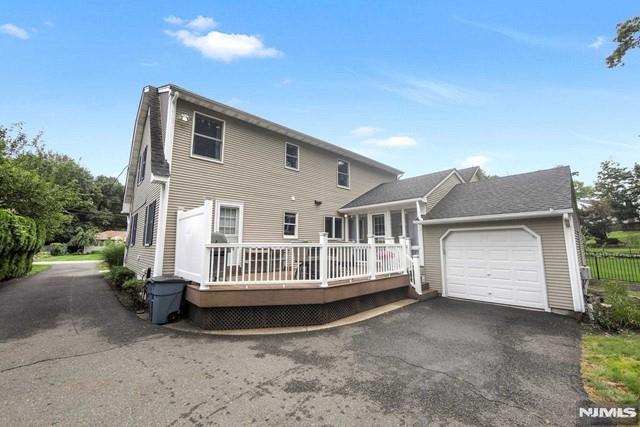 rear view of property with an attached garage, a wooden deck, and driveway