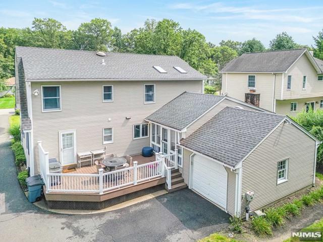 back of house with a wooden deck, a garage, driveway, and a shingled roof