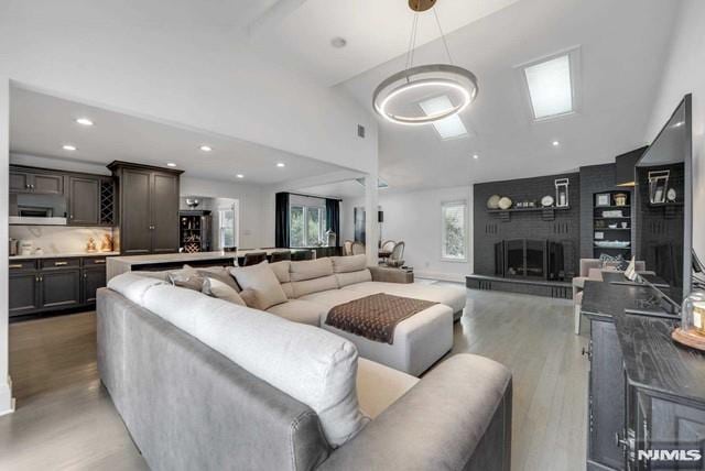 living area with a fireplace, recessed lighting, wood finished floors, and high vaulted ceiling