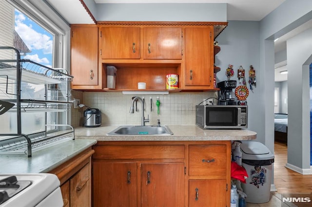 kitchen with stainless steel microwave, a sink, light countertops, open shelves, and brown cabinetry