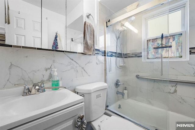 bathroom featuring backsplash, vanity, toilet, and bath / shower combo with glass door