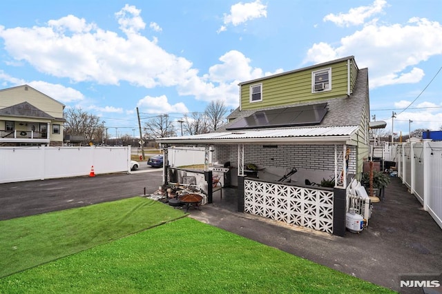 back of house featuring a yard, brick siding, fence, and roof mounted solar panels