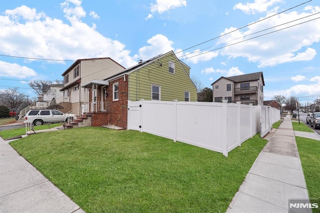 view of side of home featuring a yard, brick siding, and fence