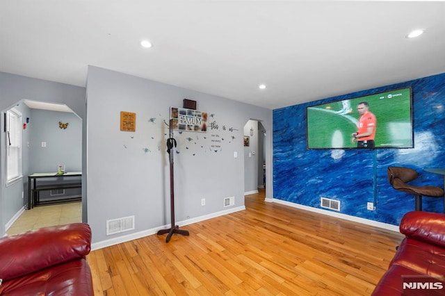 living room featuring an accent wall, arched walkways, wood-type flooring, and visible vents