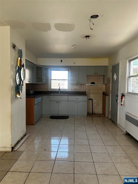 kitchen featuring dark countertops, radiator heating unit, light tile patterned floors, a wealth of natural light, and a sink