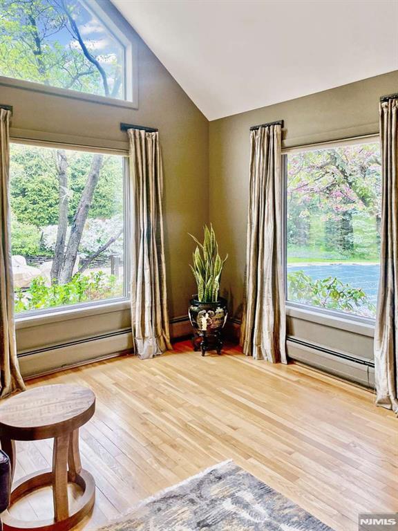 sitting room featuring lofted ceiling, a healthy amount of sunlight, a baseboard radiator, and wood finished floors