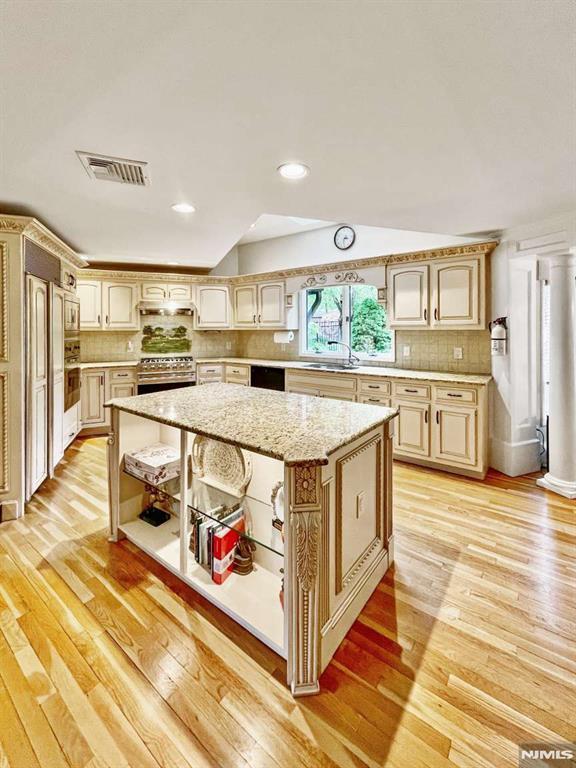 kitchen featuring stainless steel range, visible vents, a kitchen island, open shelves, and a sink