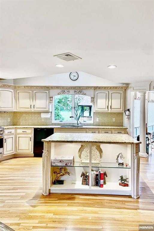 kitchen featuring light stone counters, visible vents, vaulted ceiling, light wood-type flooring, and dishwasher