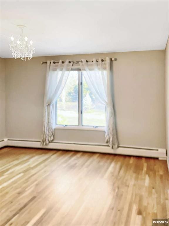 spare room with a baseboard heating unit, a chandelier, and light wood-style floors