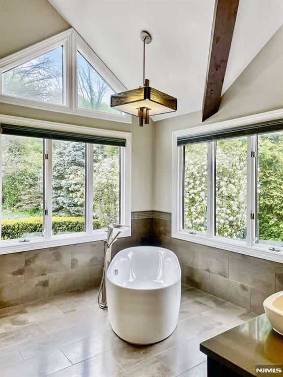 bathroom with vaulted ceiling with beams, a soaking tub, tile walls, and a healthy amount of sunlight