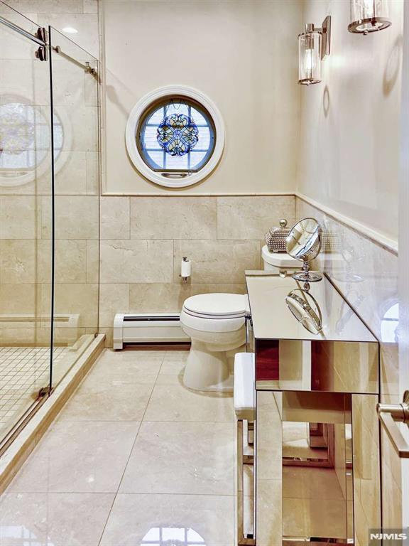 full bath featuring toilet, a baseboard radiator, tile patterned flooring, a shower stall, and tile walls