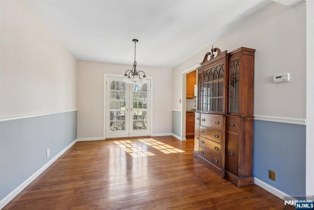 unfurnished dining area featuring dark wood-style floors, baseboards, and an inviting chandelier