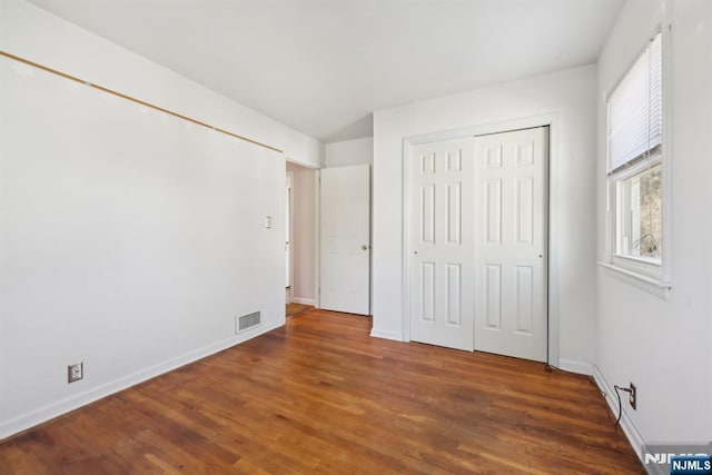 unfurnished bedroom with a closet, visible vents, baseboards, and wood finished floors