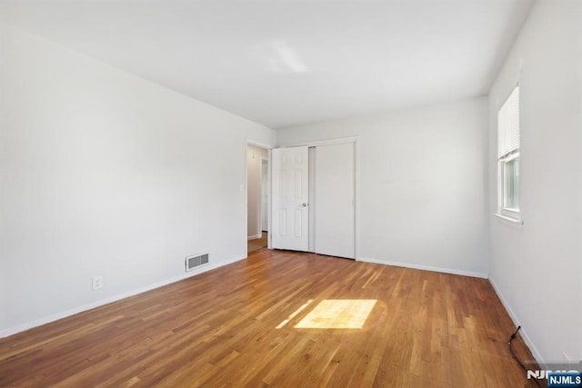 unfurnished bedroom with a closet, visible vents, baseboards, and wood finished floors