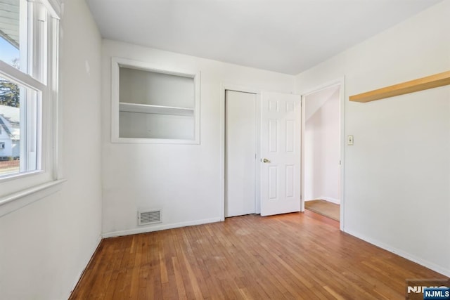 unfurnished bedroom featuring hardwood / wood-style flooring, a closet, visible vents, and baseboards