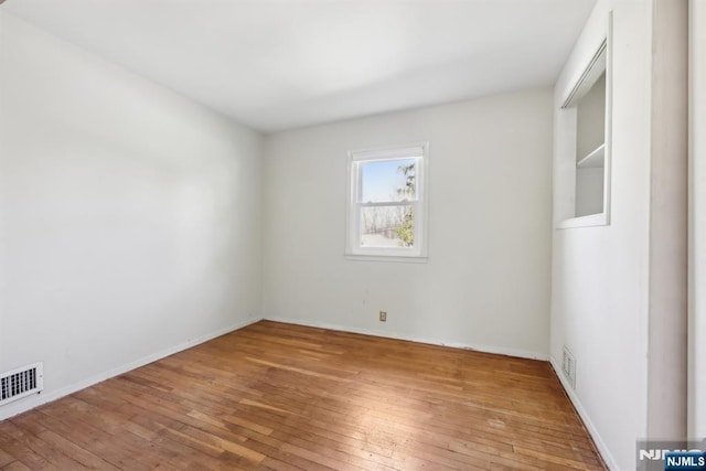 unfurnished room featuring wood-type flooring, visible vents, and baseboards