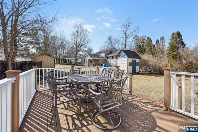 wooden terrace featuring an outbuilding, a storage unit, outdoor dining area, and a fenced backyard