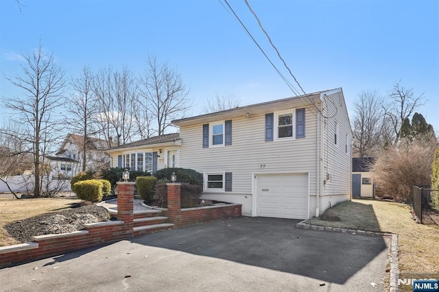 split level home featuring aphalt driveway, fence, and an attached garage