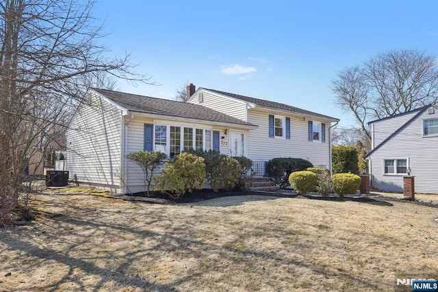 split level home with a front yard, a chimney, and central air condition unit