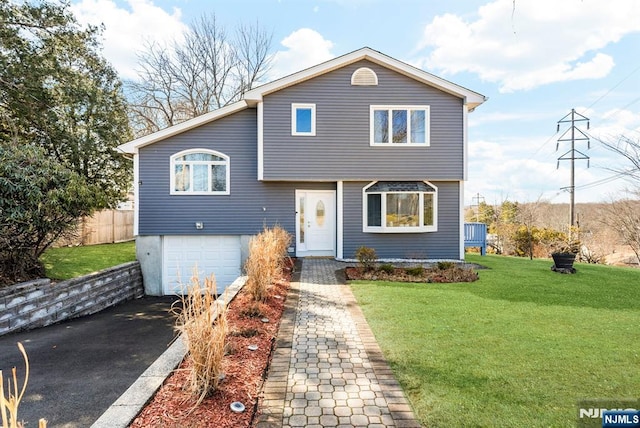 split level home featuring an attached garage, fence, aphalt driveway, and a front yard