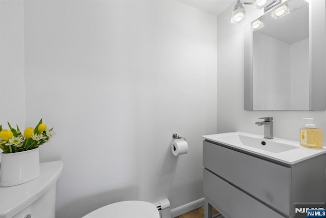 half bath featuring toilet, baseboards, a baseboard heating unit, and vanity