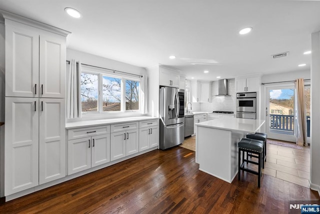 kitchen featuring visible vents, wall chimney exhaust hood, a kitchen breakfast bar, stainless steel appliances, and white cabinetry