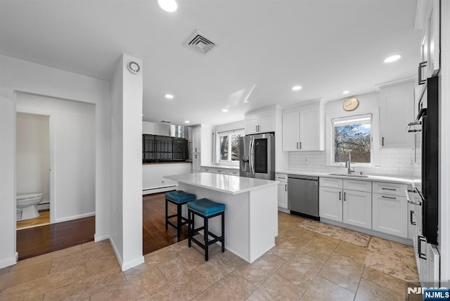 kitchen with tasteful backsplash, a sink, stainless steel appliances, a baseboard heating unit, and a wealth of natural light