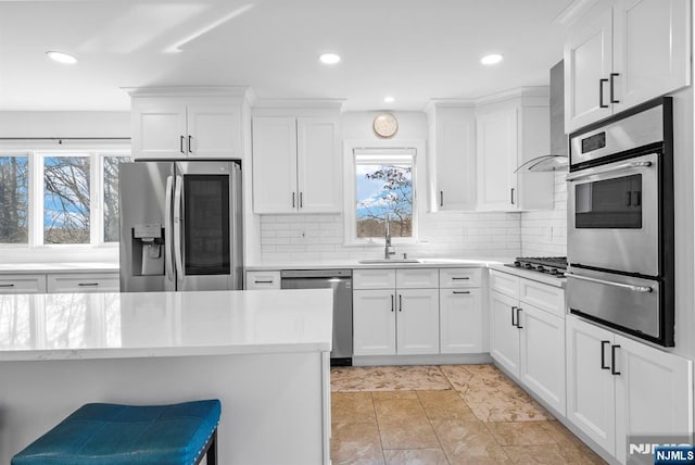 kitchen featuring a sink, light countertops, wall chimney range hood, appliances with stainless steel finishes, and a warming drawer