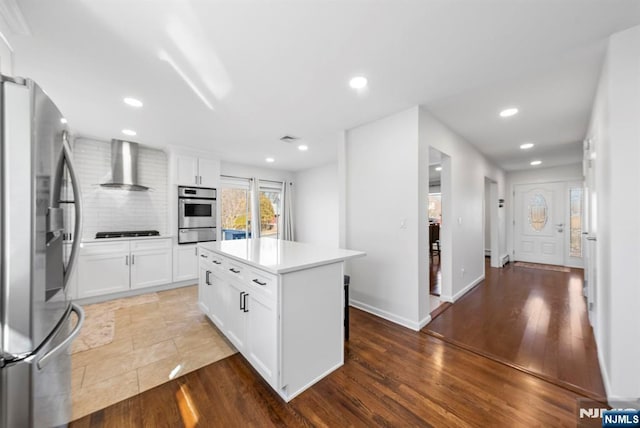 kitchen with stainless steel appliances, wood finished floors, white cabinetry, wall chimney exhaust hood, and tasteful backsplash