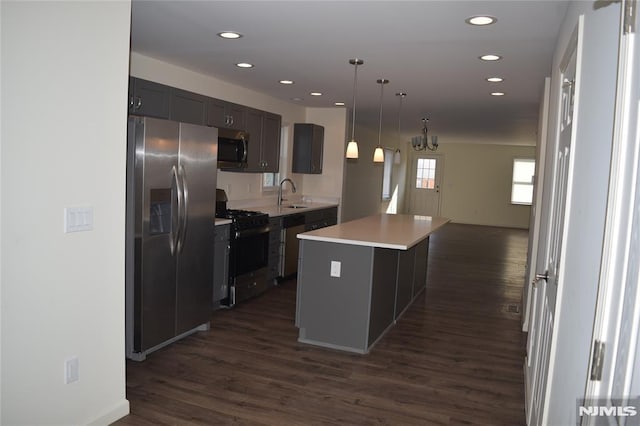 kitchen with a sink, a kitchen island, dark wood-style floors, appliances with stainless steel finishes, and light countertops