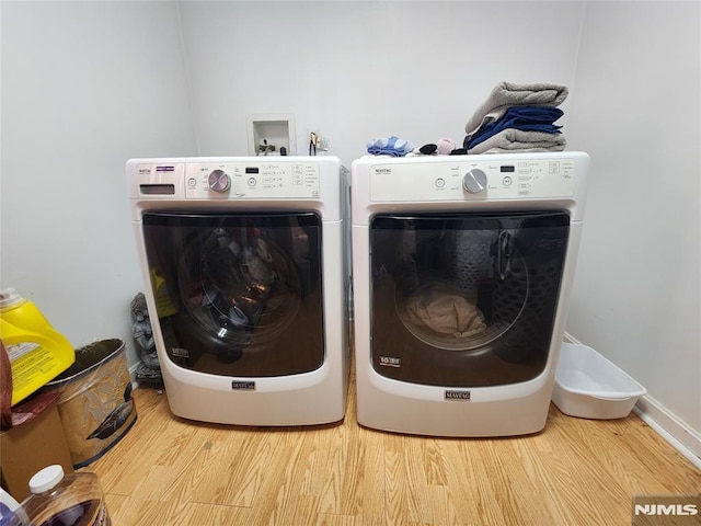 clothes washing area with washer and dryer, laundry area, baseboards, and wood finished floors