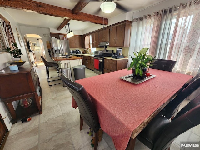 dining area with arched walkways, beam ceiling, and a ceiling fan