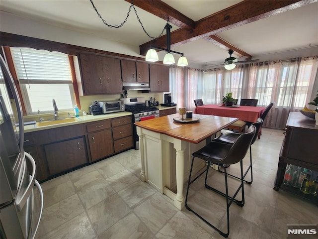 kitchen with stainless steel appliances, a sink, dark brown cabinets, beamed ceiling, and under cabinet range hood