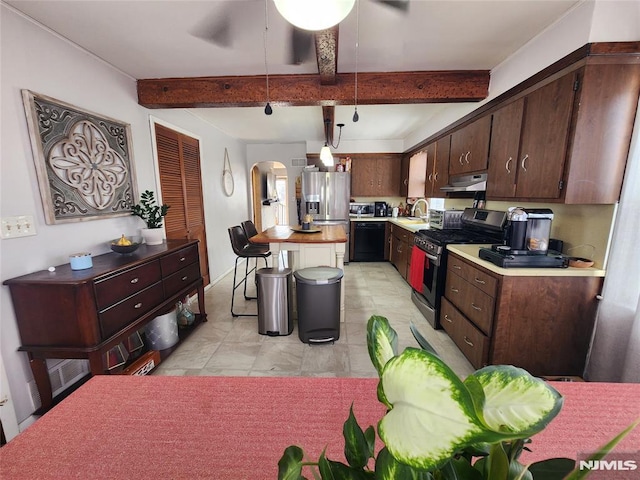 kitchen featuring arched walkways, under cabinet range hood, light countertops, appliances with stainless steel finishes, and beam ceiling